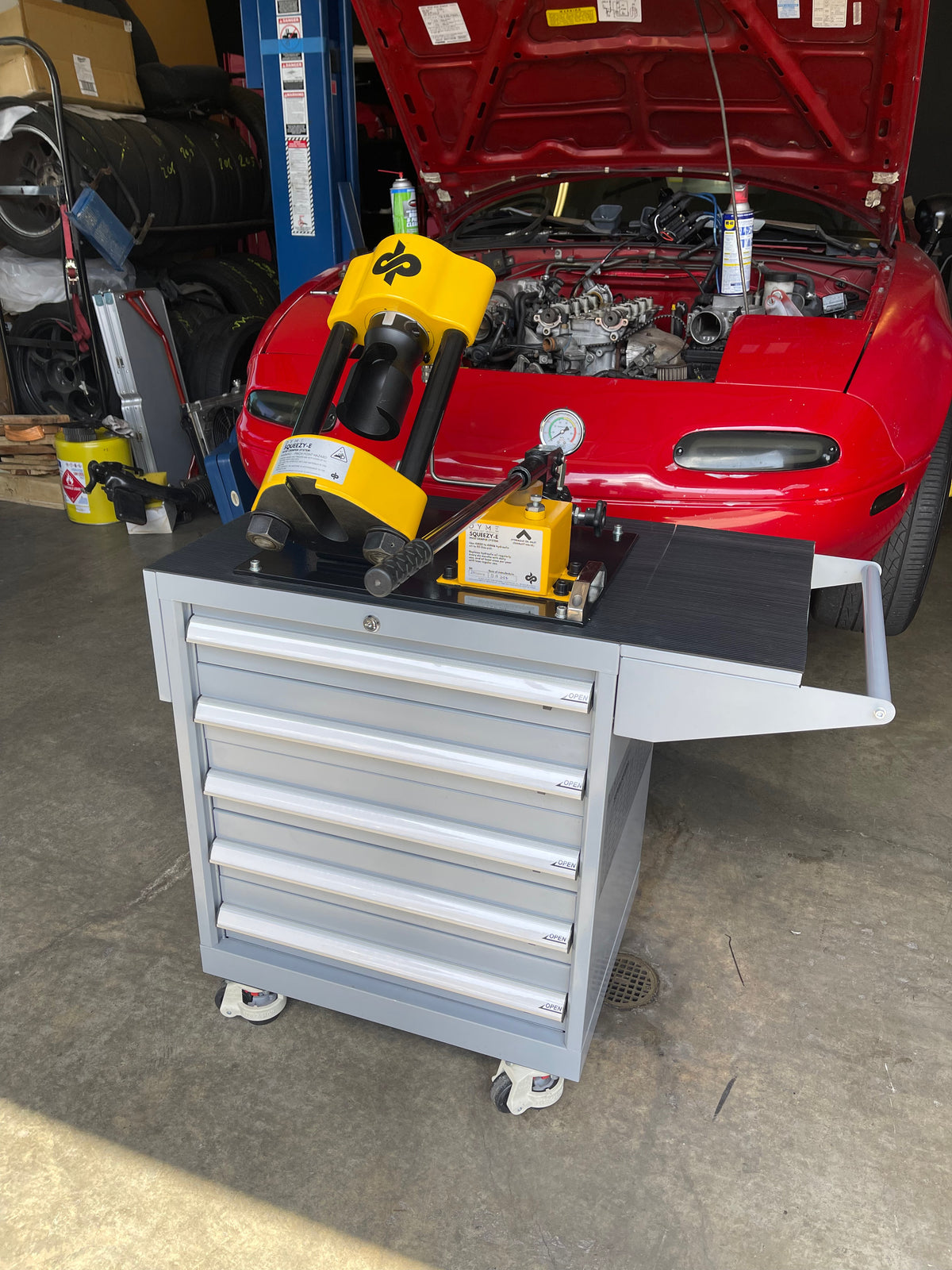 Dyme PRO hose crimper on a tool cart in front of a red car